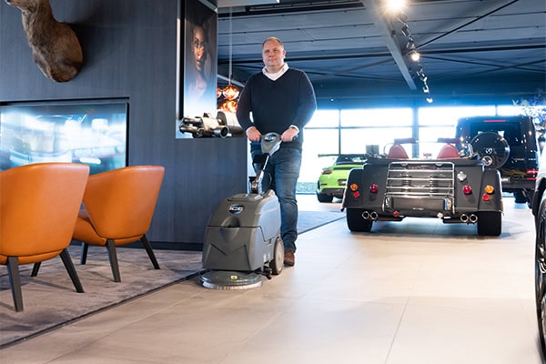 Schuifluid robot reinigen vloer in autodealer met automaten en luxe auto's op de achtergrond.