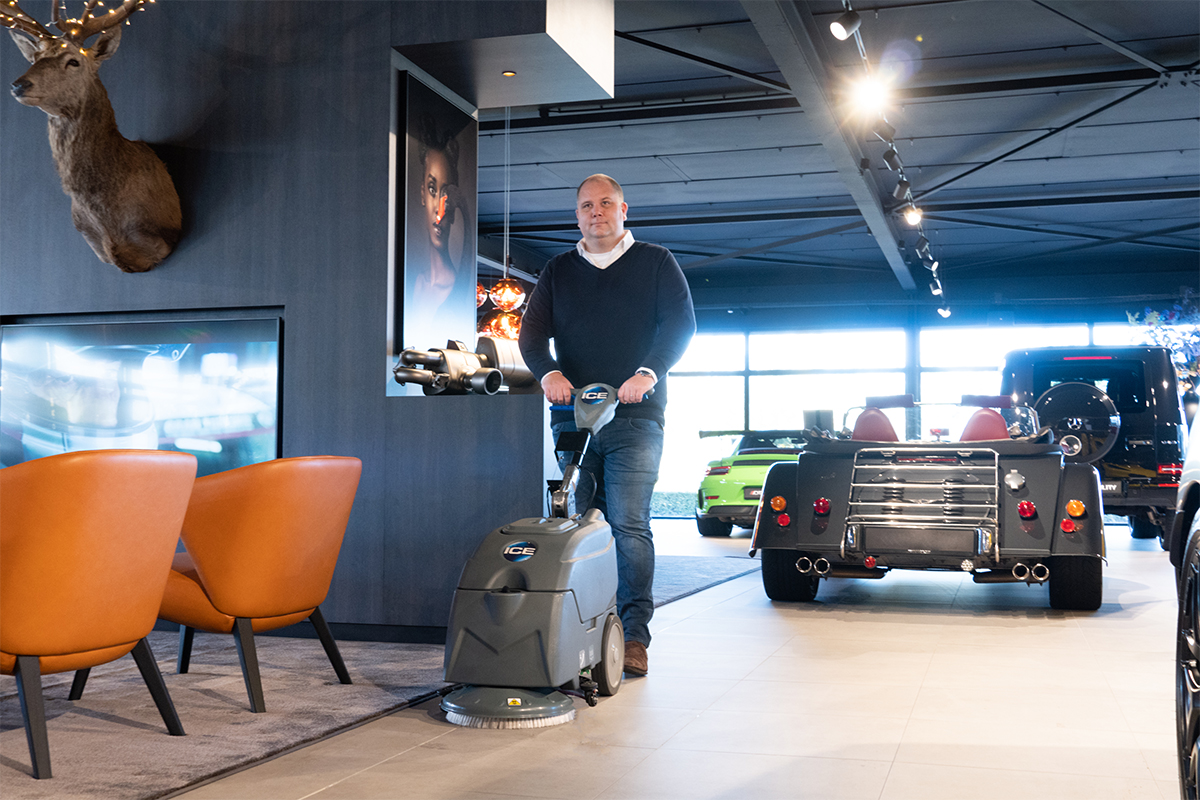 Schuifluid robot reinigen vloer in autodealer met automaten en luxe auto's op de achtergrond.